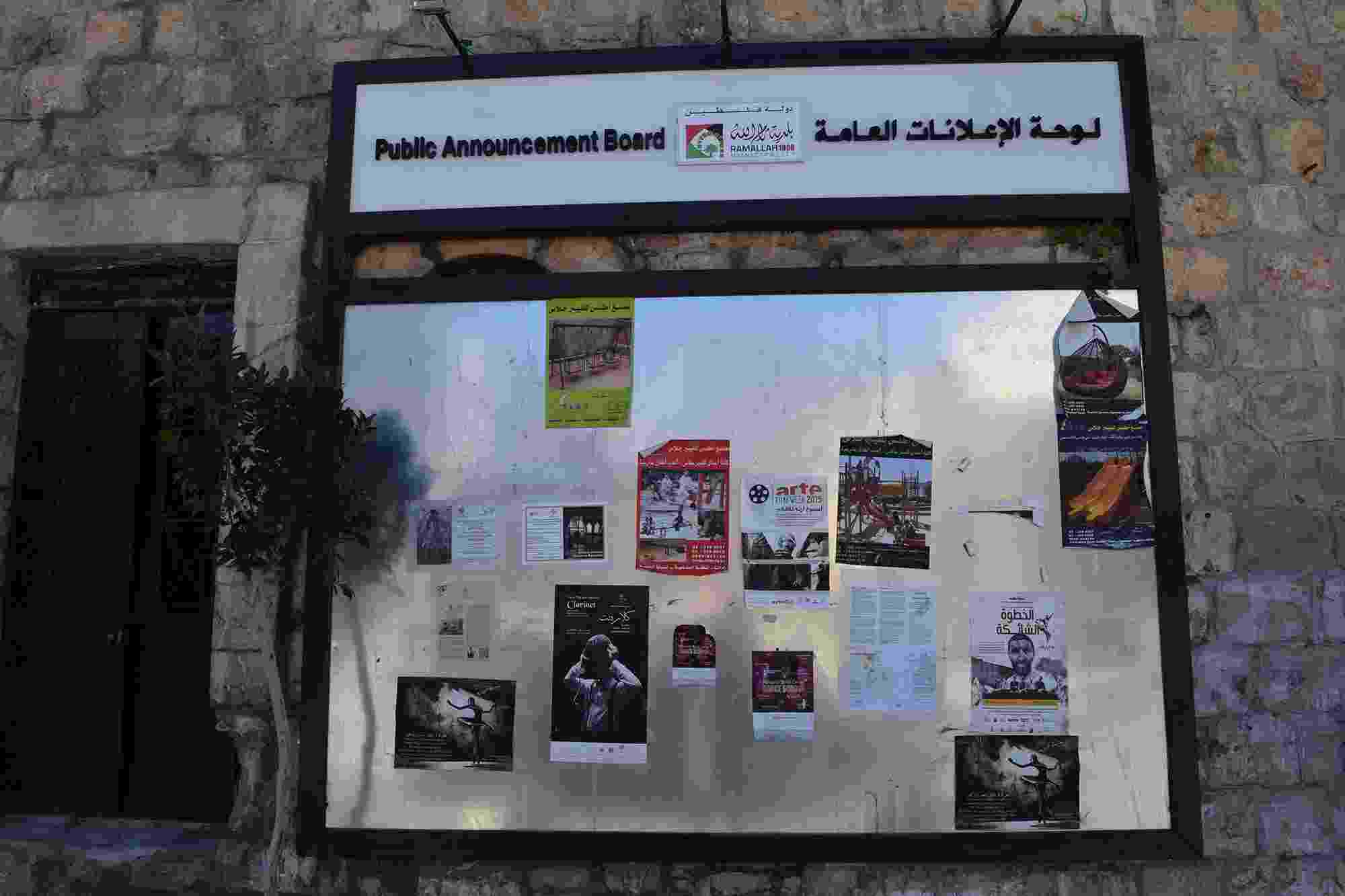 A noticeboard fixed to a stone wall, filled with announcements, adverts, and posters
